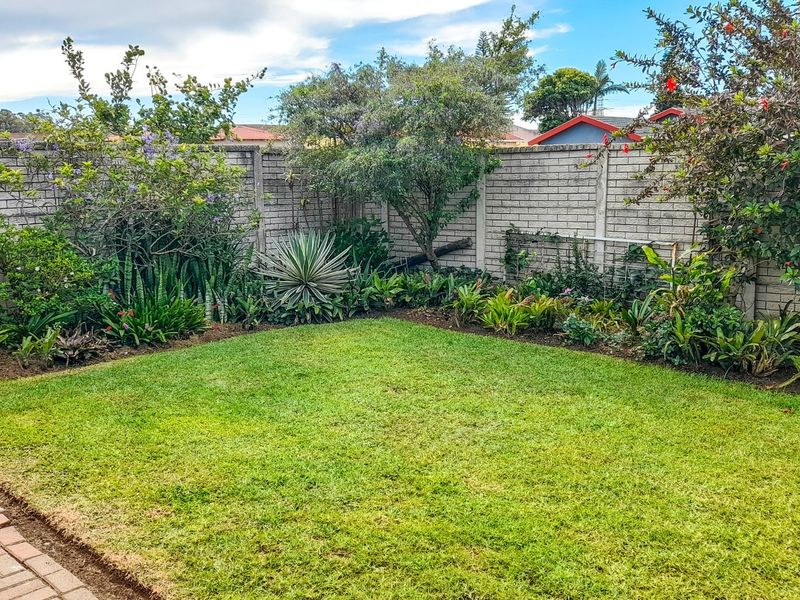 A well-maintained private rear garden featuring a lush green lawn, established perimeter landscaping, and a solid brick boundary wall.