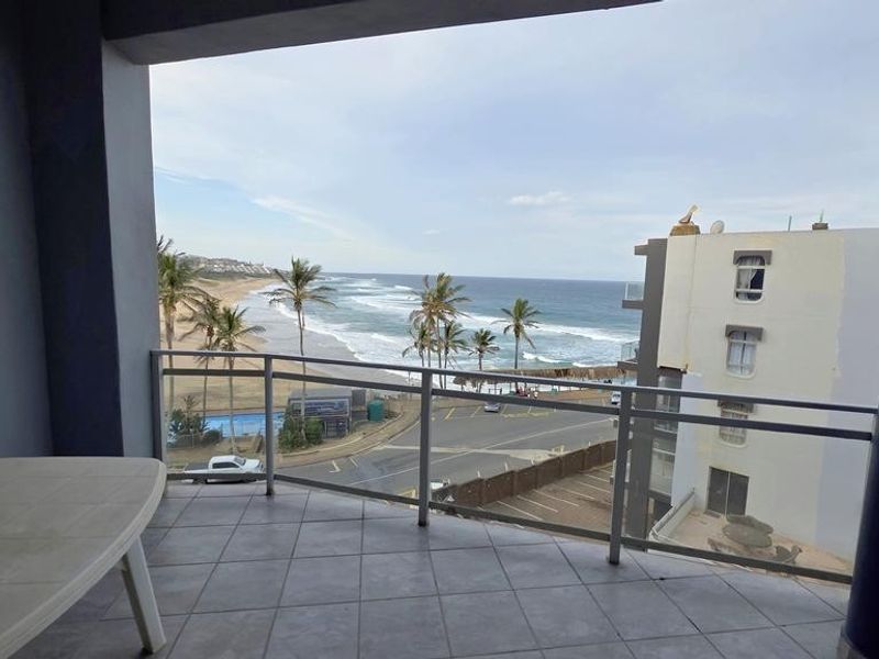 Covered balcony featuring tiled flooring and metal railings, offering expansive views of the coastline and beach.