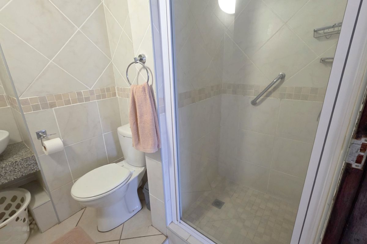 A functional bathroom featuring a glass-enclosed shower with a grab bar, a toilet, and a vanity basin with tiled walls.