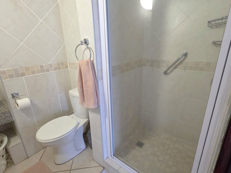 A functional bathroom featuring a glass-enclosed shower with a grab bar, a toilet, and a vanity basin with tiled walls.