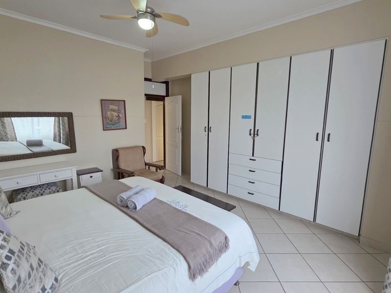 A spacious bedroom featuring large built-in wardrobes with white cabinetry, tiled flooring, and a ceiling fan.