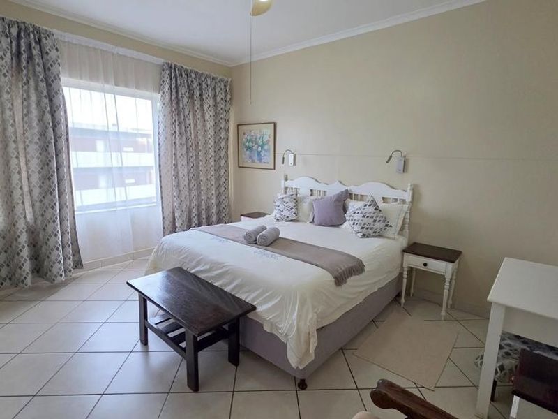 A well-lit bedroom featuring tiled flooring, large windows with curtains, and a neutral color palette, providing a comfortable and functional living space.