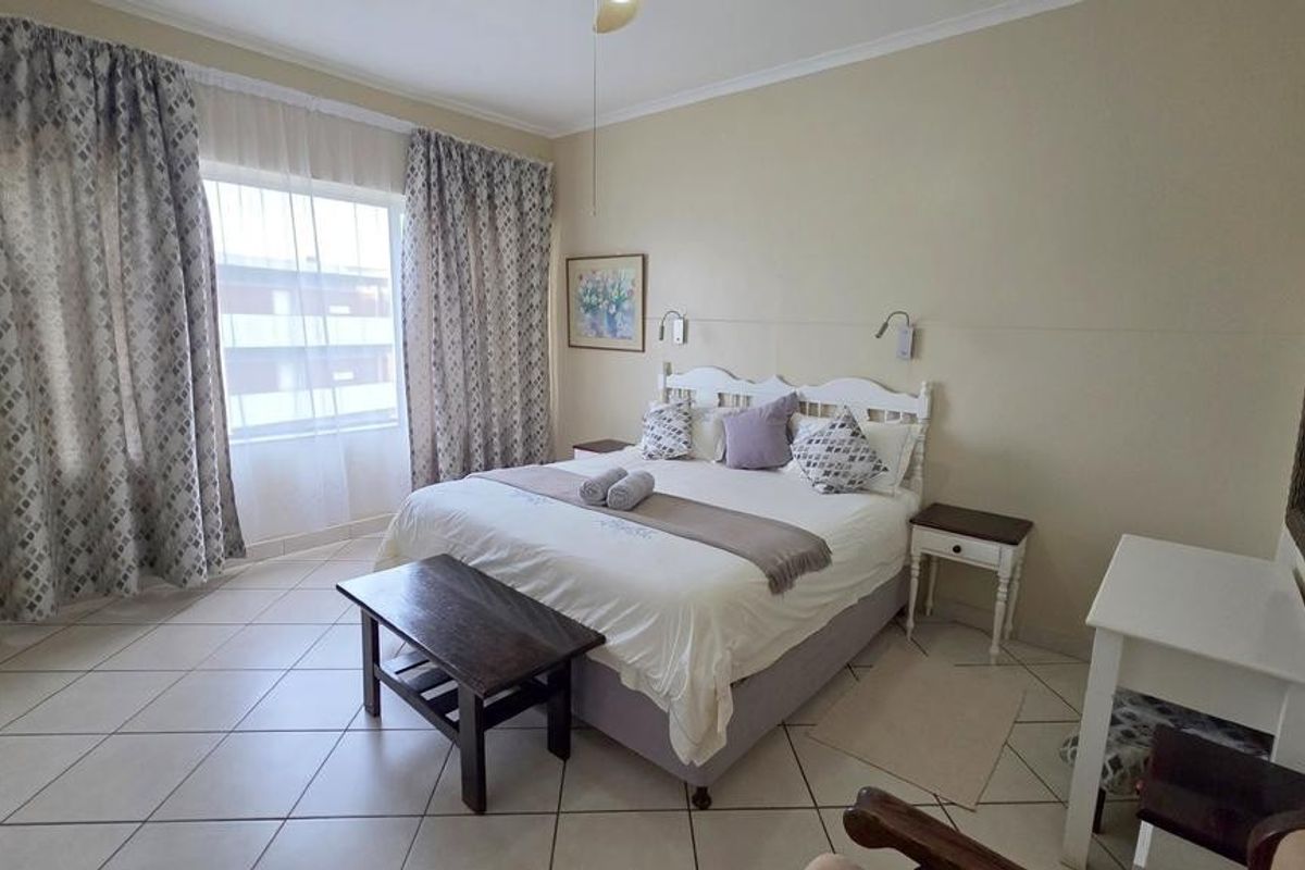 A well-lit bedroom featuring tiled flooring, large windows with curtains, and a neutral color palette, providing a comfortable and functional living space.
