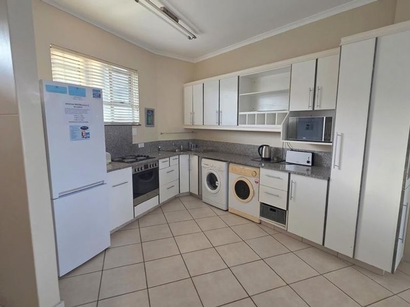 Functional kitchen featuring granite countertops, built-in oven, hob, extractor fan, and integrated laundry appliance space with ample cabinetry for storage.