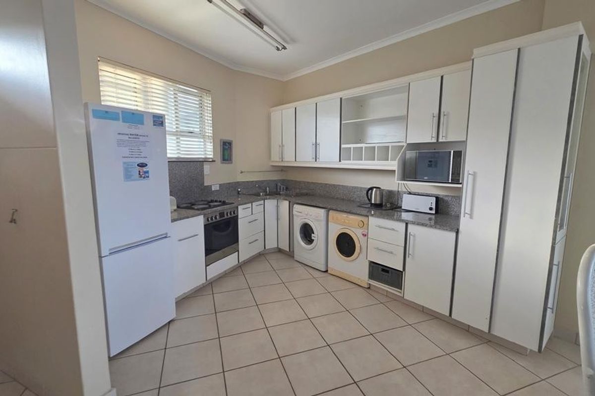 Functional kitchen featuring granite countertops, built-in oven, hob, extractor fan, and integrated laundry appliance space with ample cabinetry for storage.