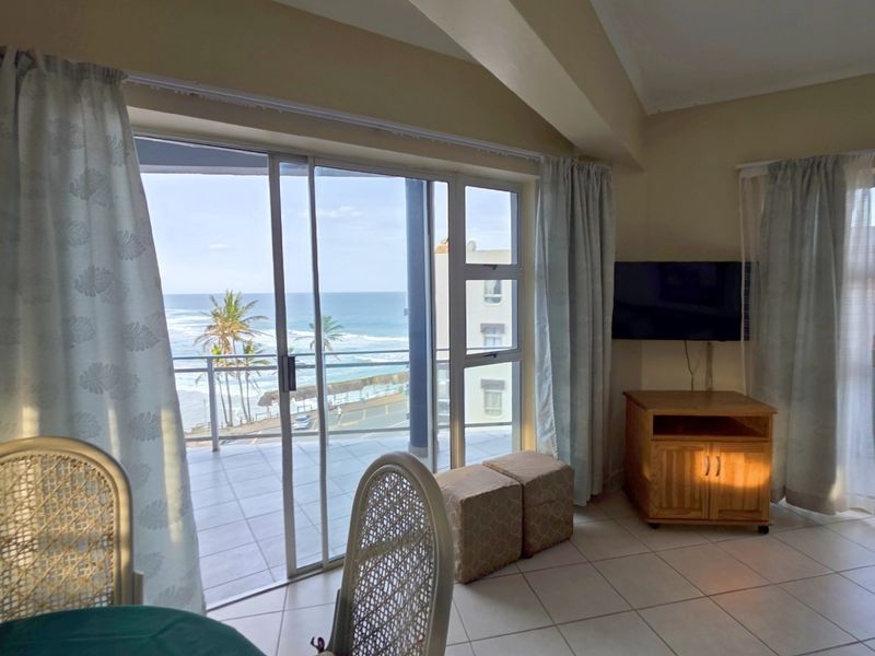 Open plan living area featuring tiled flooring and large sliding glass doors leading to a balcony with ocean views.