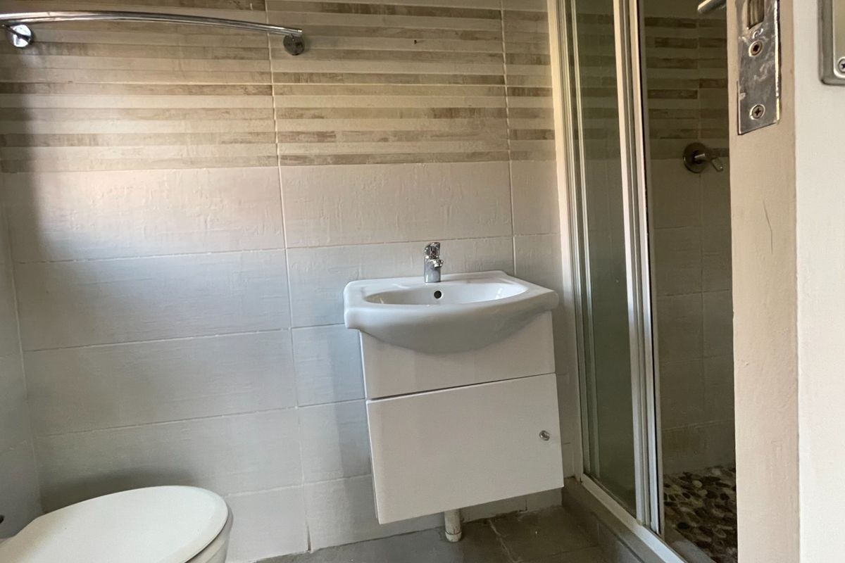 A functional bathroom featuring a wall-mounted vanity, a tiled shower enclosure, and neutral wall tiling.