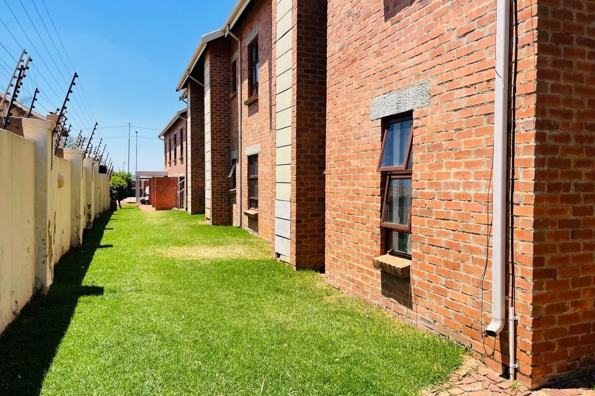 Side view of the apartment building featuring exposed brick facade, grass lawn, and a perimeter wall with security fencing.
