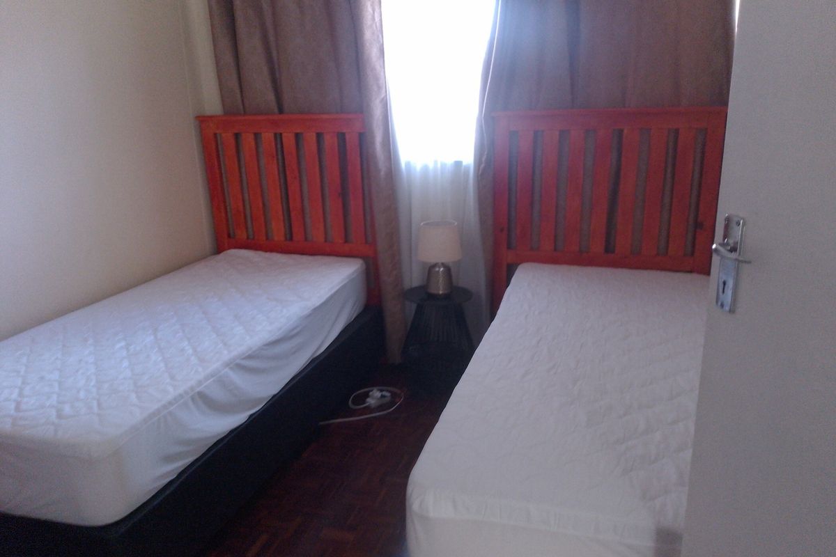 A bedroom featuring dark wood parquet flooring and a window with curtains.