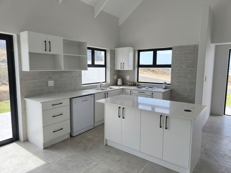 Modern kitchen featuring white cabinetry, stone countertops, a central island, subway tile backsplash, and vaulted ceilings with ample natural light.