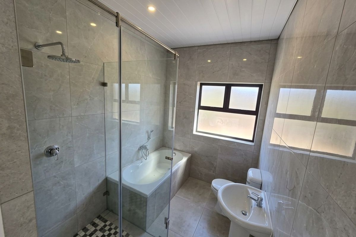 Modern bathroom featuring a glass-enclosed shower, built-in bathtub, pedestal basin, and toilet, finished with neutral floor-to-ceiling tiles and recessed lighting.