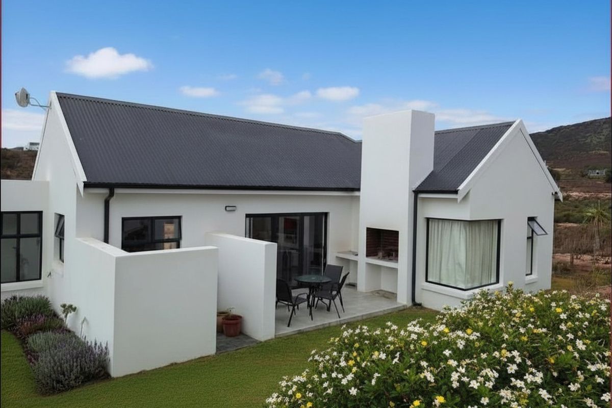 Rear view of a modern white house featuring a corrugated metal roof, a built-in braai area, and a paved patio overlooking the garden.
