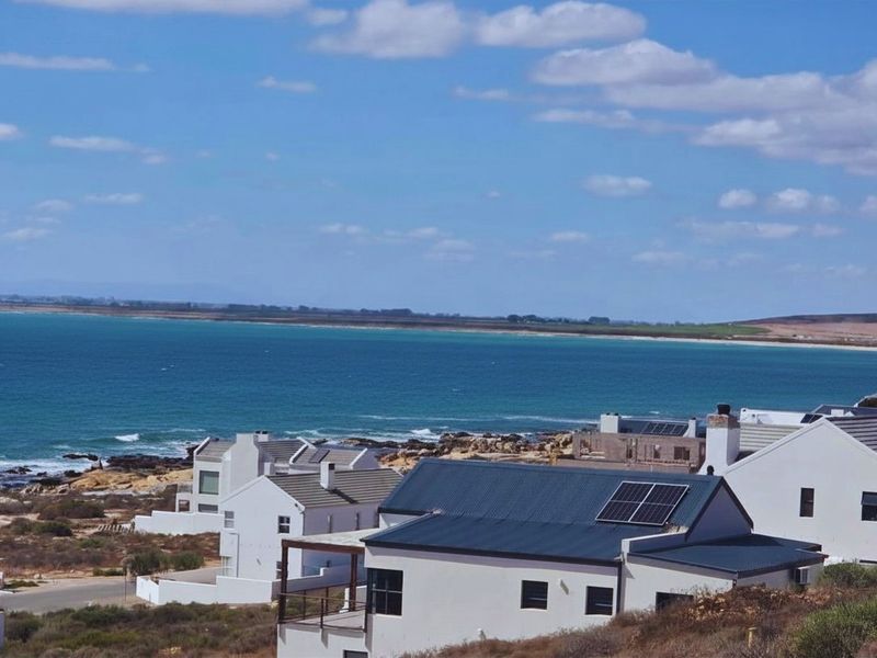 Elevated coastal view overlooking residential properties with solar panel installations and ocean scenery.