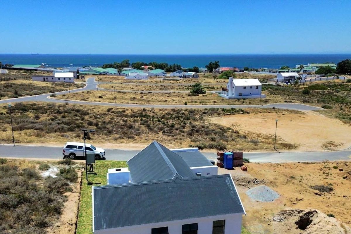 Aerial view of a coastal residential property featuring a metal roof, surrounding paved roads, and distant ocean views in a developing estate.