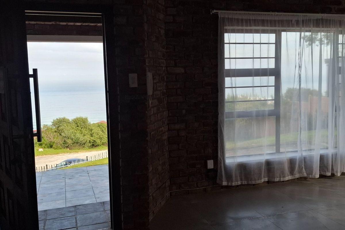 Living area featuring exposed brick walls, tiled flooring, and large windows with direct access to an outdoor patio area with ocean views.