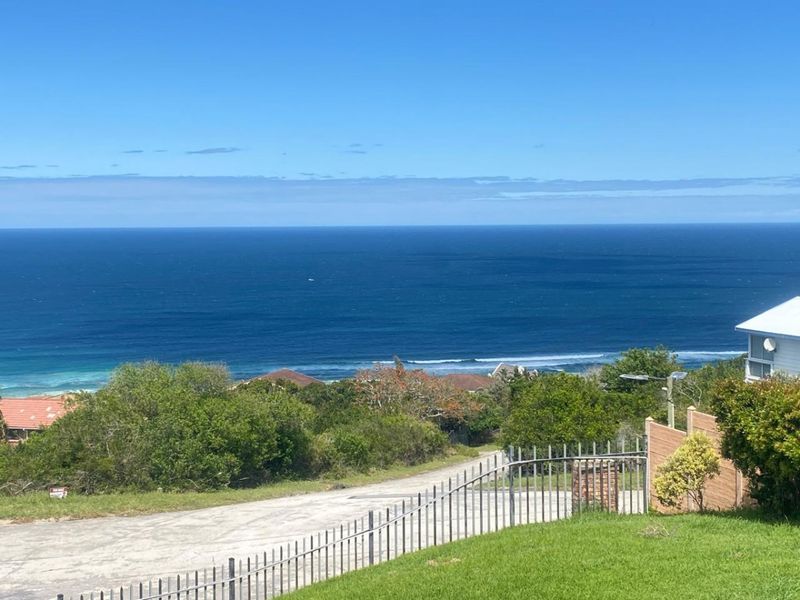A scenic elevated view overlooking the coastline and ocean, featuring a landscaped lawn and perimeter fencing.