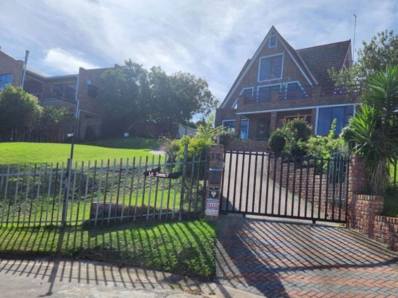 A street-level view of a multi-story brick house featuring a steep pitched roof, paved driveway, and secure metal gate entrance.