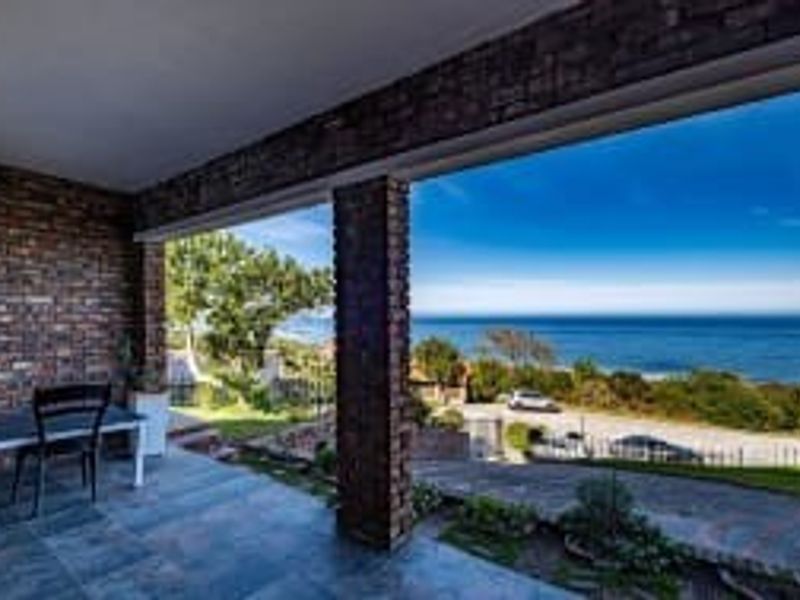 A covered patio featuring exposed brick pillars and stone flooring, offering expansive ocean views and direct access to the garden.