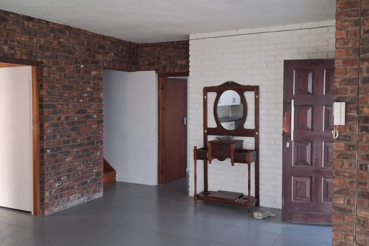An interior view of a living area featuring exposed brick walls, painted brick accents, and tiled flooring with multiple doorways leading to other rooms.