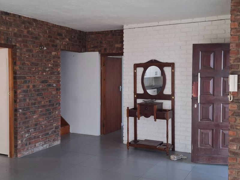 An interior view of a living area featuring exposed brick walls, painted brick accents, and tiled flooring with multiple doorways leading to other rooms.