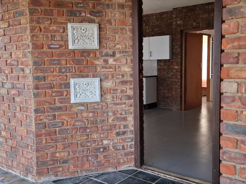 View from a covered patio looking into an open plan living area with exposed brick walls and tiled flooring.
