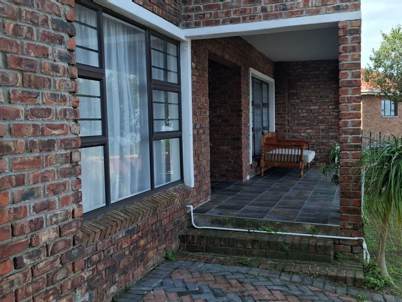 A covered patio area featuring exposed brick walls, dark tiled flooring, and large windows, providing a sheltered outdoor space.