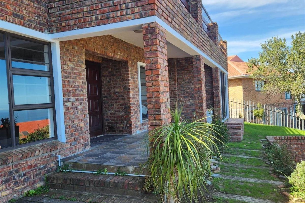 A view of the exterior facade featuring face brick construction, a covered patio area, and a landscaped garden with paved pathways.