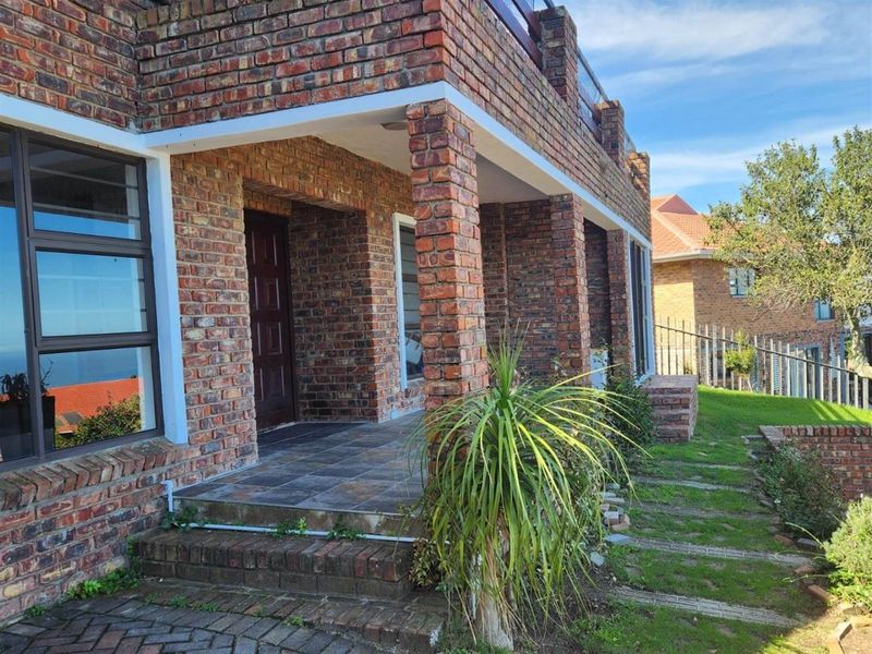 A view of the exterior facade featuring face brick construction, a covered patio area, and a landscaped garden with paved pathways.