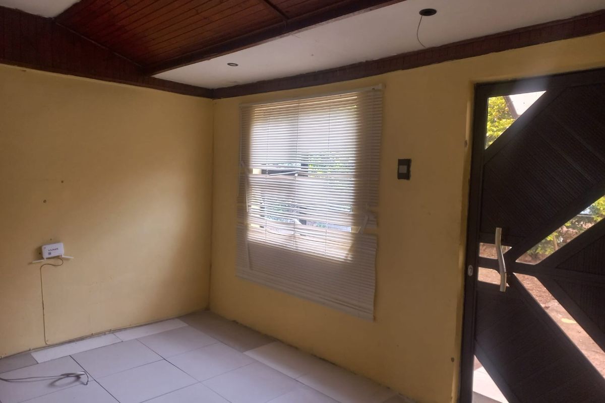 An empty room featuring tiled flooring, a timber-paneled ceiling, and a decorative entrance door, currently requiring cosmetic updates and minor repairs.