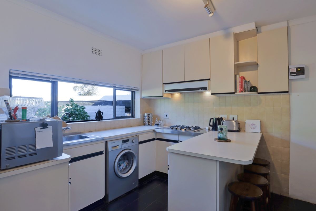 A functional kitchen featuring built-in cabinetry, a gas hob with extractor fan, tiled splashback, and a convenient breakfast bar area.