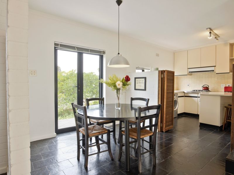Open-plan kitchen and dining area featuring dark tiled flooring, neutral cabinetry, and direct access to the outdoors through a glass door.