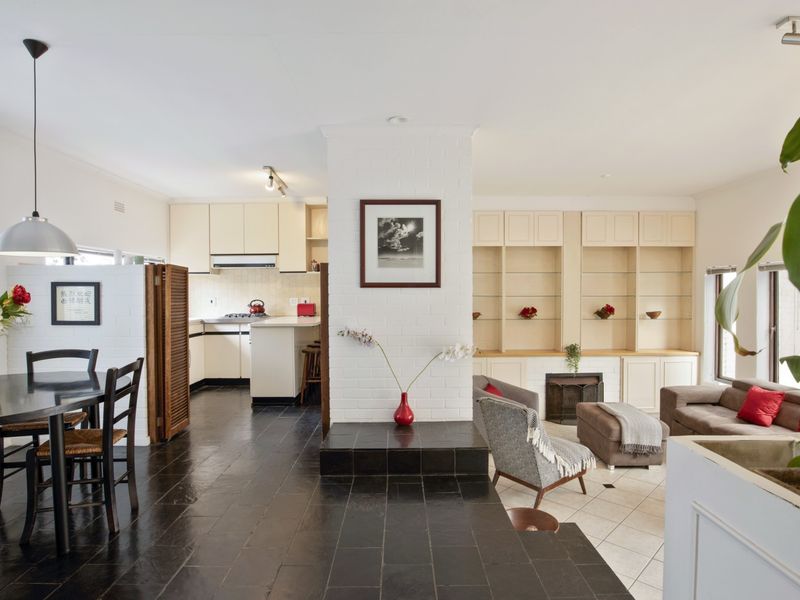 Open-plan living and dining area featuring a central fireplace, built-in shelving, and a functional kitchen with integrated cabinetry and stone tile flooring.