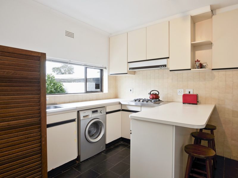 Functional kitchen featuring built-in cabinetry, gas hob, extractor fan, tiled backsplash, and a breakfast counter with integrated laundry space.