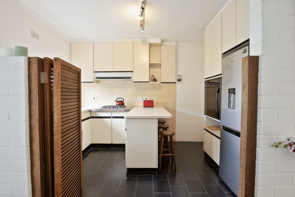 Functional kitchen featuring built-in cabinetry, gas cooktop, integrated oven, and a breakfast bar with tiled flooring.