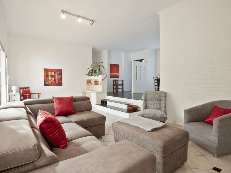 Spacious living room featuring tiled flooring, a painted brick feature wall, and a split-level layout with access to outdoor areas via sliding glass doors.