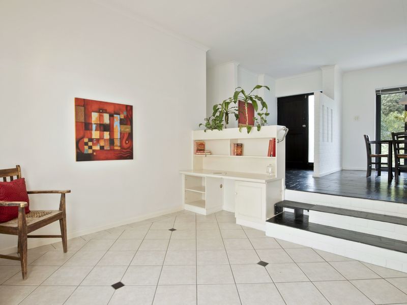 Open plan living area featuring a built-in desk, tiled flooring, and a stepped transition leading to a dining space with garden views.