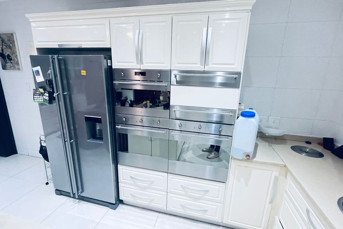 A modern kitchen featuring white cabinetry, integrated stainless steel ovens, and a large double-door refrigerator with a sleek, clean finish.