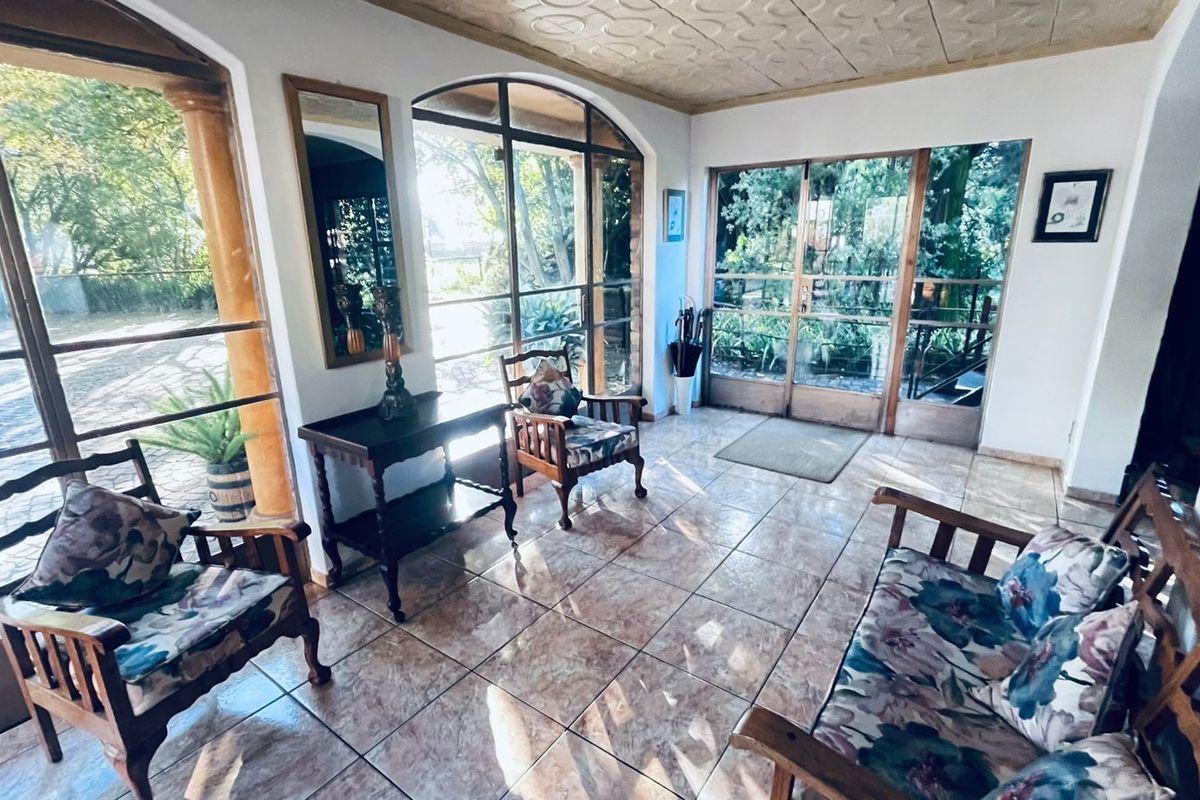 A bright sunroom or entrance area featuring large arched windows, tiled flooring, and direct access to the garden.