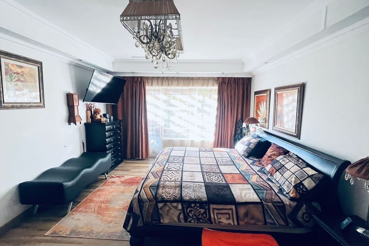 A spacious bedroom featuring crown molding, recessed ceiling lighting, and large windows with curtains, providing a comfortable and well-lit sleeping area.