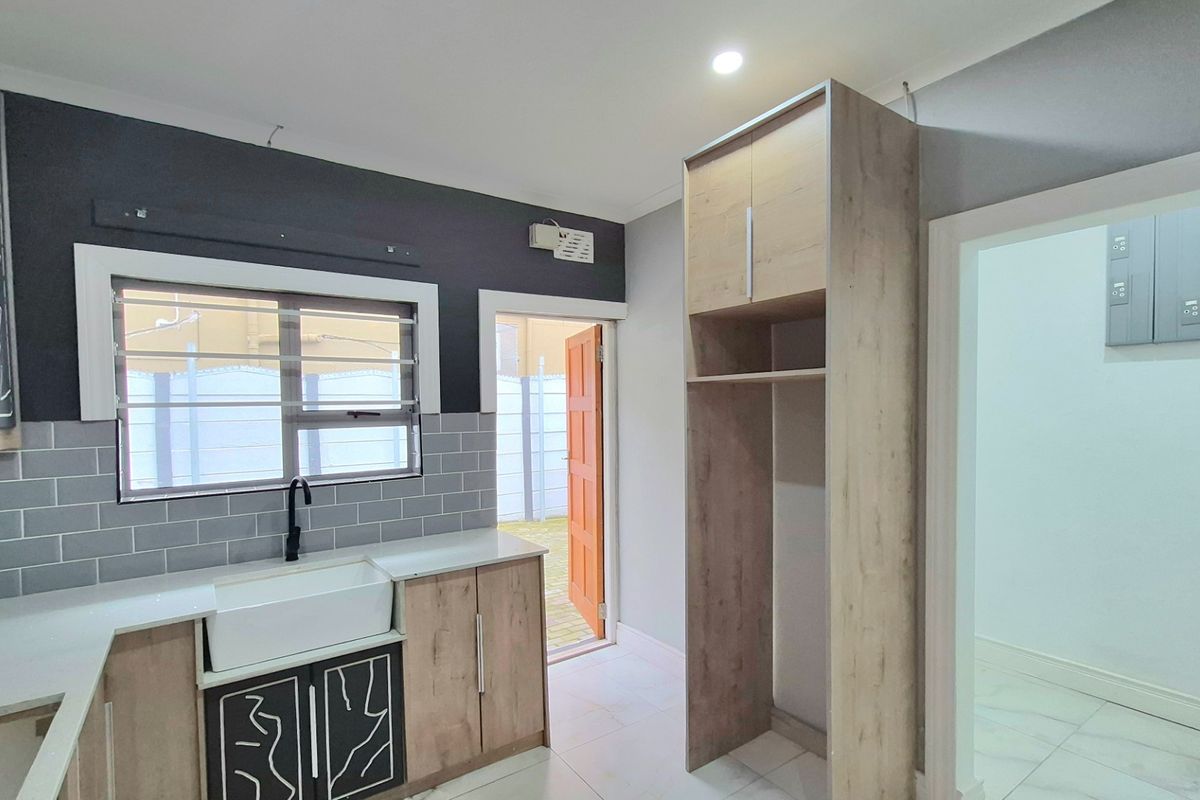 Modern kitchen featuring light wood cabinetry, a farmhouse-style sink, subway tile backsplash, and a dedicated tall pantry unit with direct outdoor access.