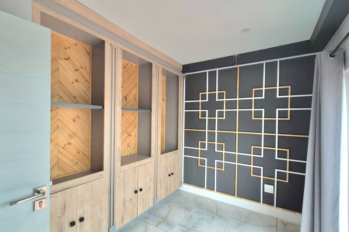 A bedroom featuring custom built-in wooden cabinetry with herringbone detailing and a decorative geometric feature wall with integrated electrical outlets.