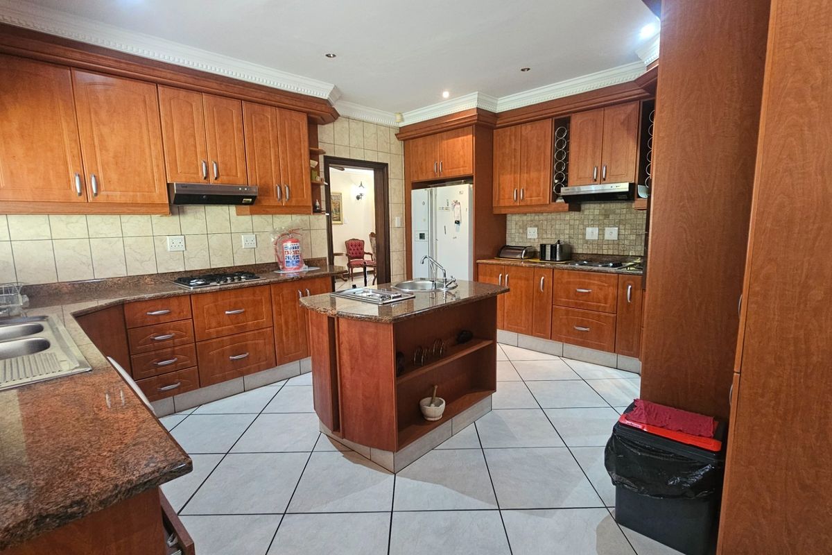 Spacious kitchen featuring extensive wooden cabinetry, granite countertops, a central island with a sink, and tiled flooring throughout.