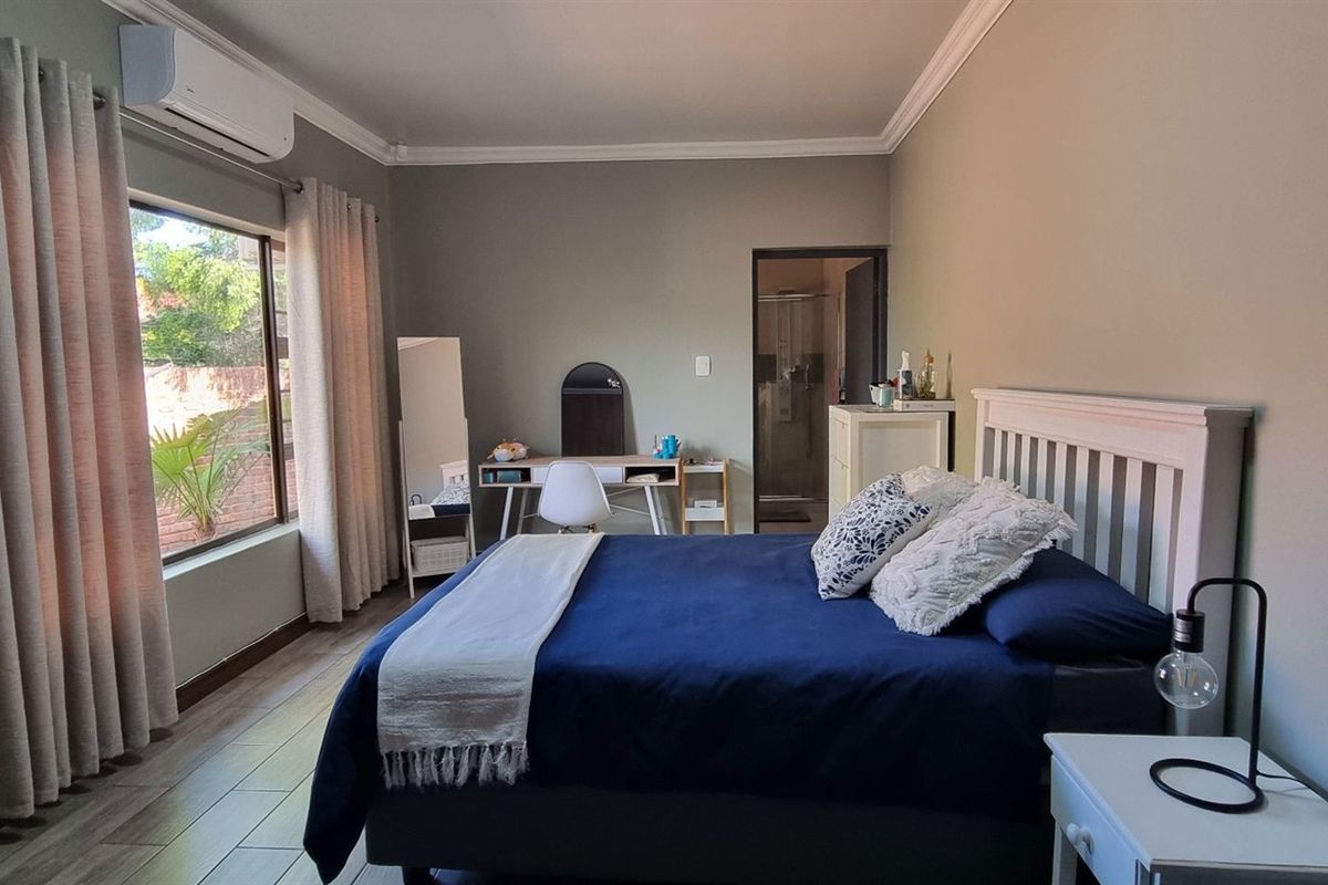 A well-maintained bedroom featuring tiled flooring, a wall-mounted air conditioning unit, and an en-suite bathroom access.