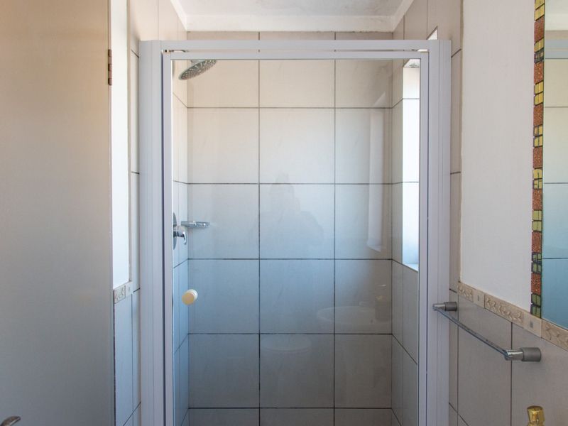 A functional bathroom featuring a glass-enclosed shower with tiled walls and a wall-mounted mirror with decorative mosaic tile trim.
