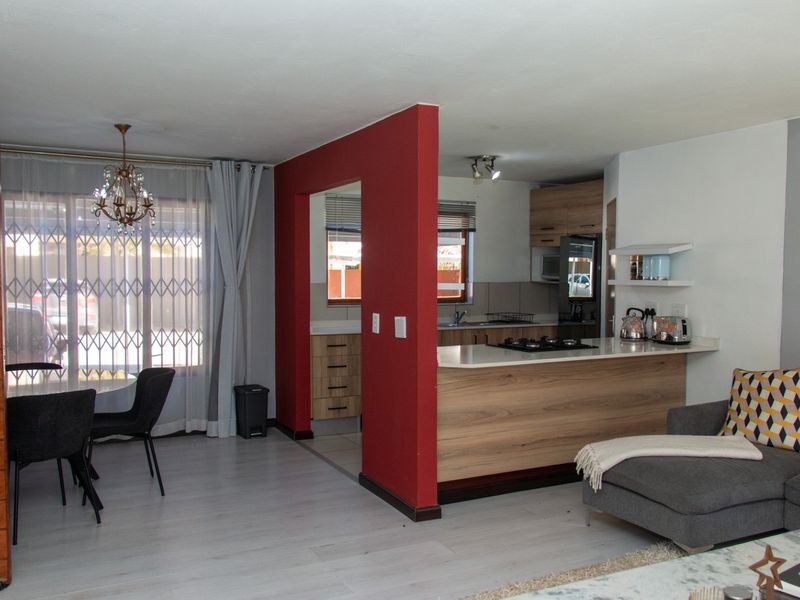 Open-plan living area featuring a modern kitchen with wood-finish cabinetry, breakfast bar, and integrated gas hob, flowing into a dining space with sliding doors.