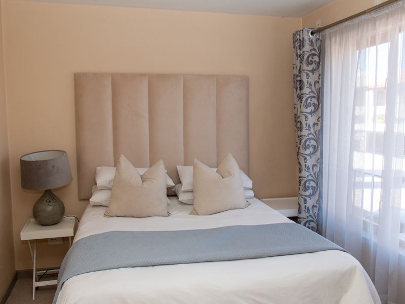 A cozy bedroom featuring neutral wall tones, a built-in headboard, and natural light provided by a window with patterned curtains.