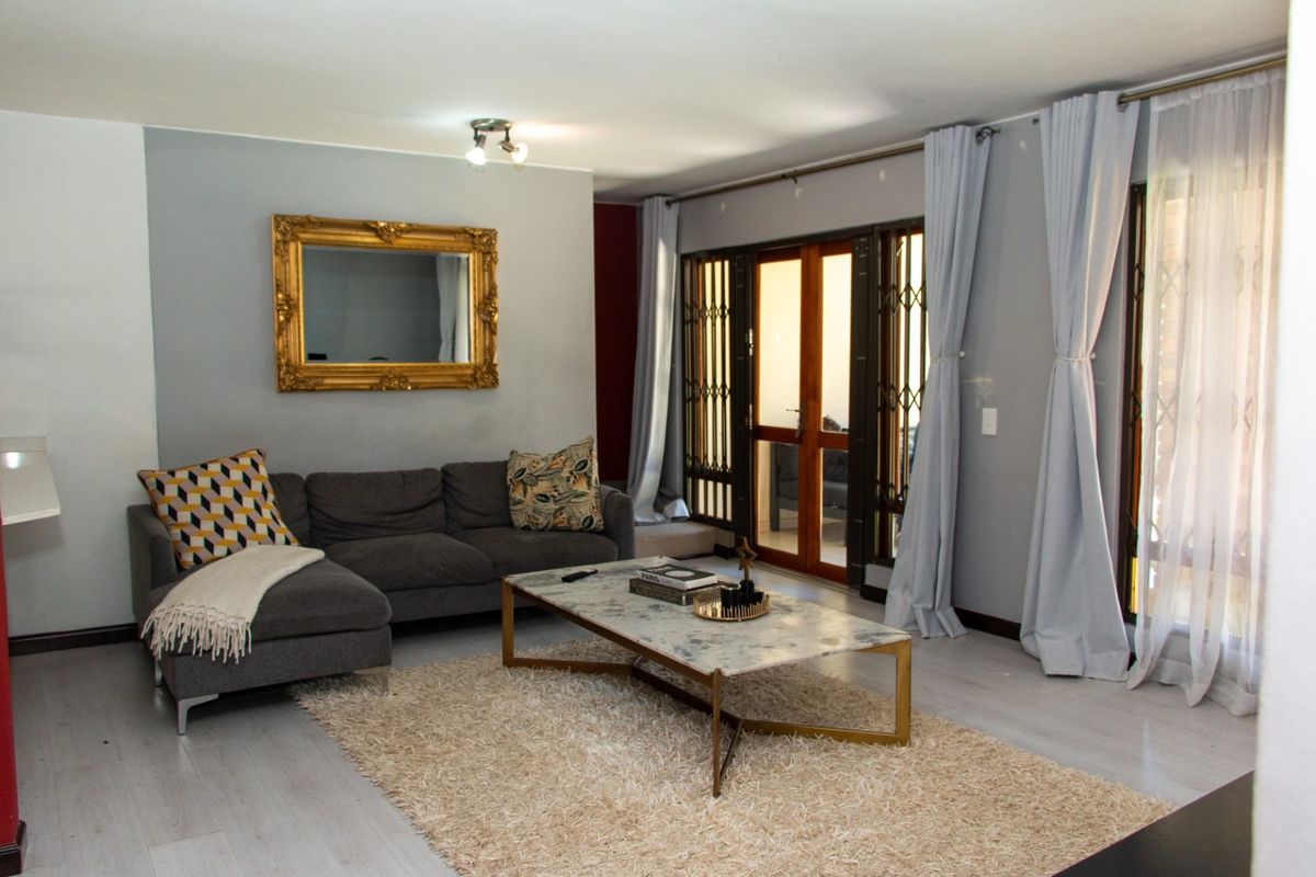 A well-maintained living room featuring light-toned laminate flooring, neutral grey walls, and direct access to an outdoor area through security-gated glass doors.