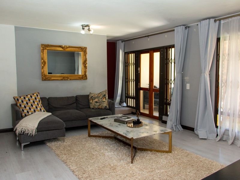 A well-maintained living room featuring light-toned laminate flooring, neutral grey walls, and direct access to an outdoor area through security-gated glass doors.