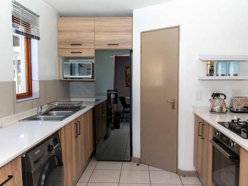 A functional kitchen featuring light wood cabinetry, stone-look countertops, a built-in gas hob, oven, and integrated space for laundry appliances.