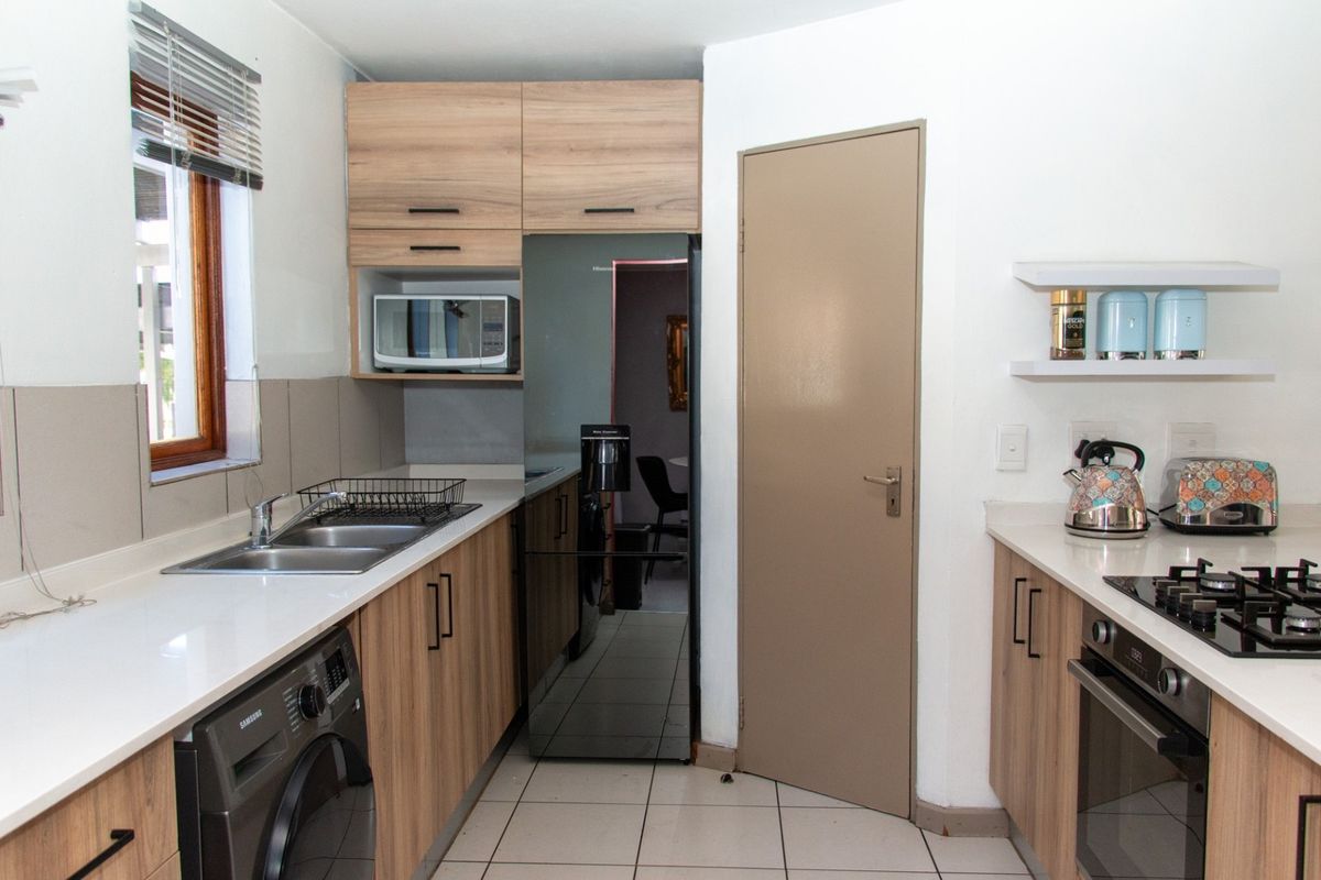 A functional kitchen featuring light wood cabinetry, stone-look countertops, a built-in gas hob, oven, and integrated space for laundry appliances.